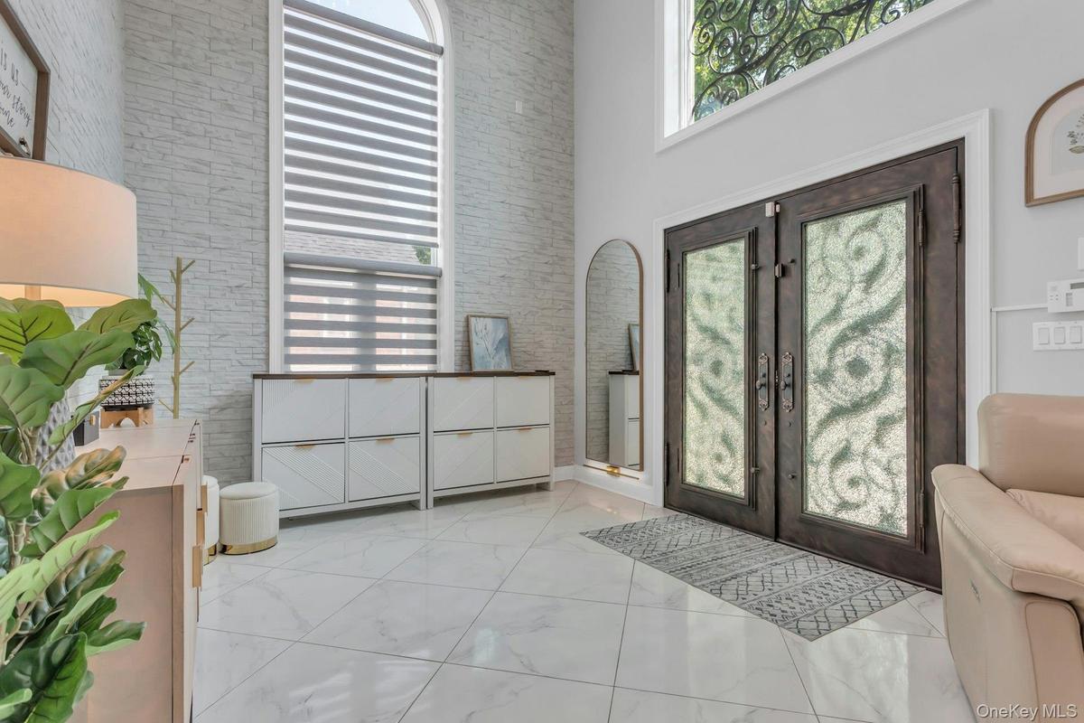 Double iron entry doors featuring crushed glass panels, stacked stone accent wall, over-sized elliptical windows providing a warm ambiance of light, e
