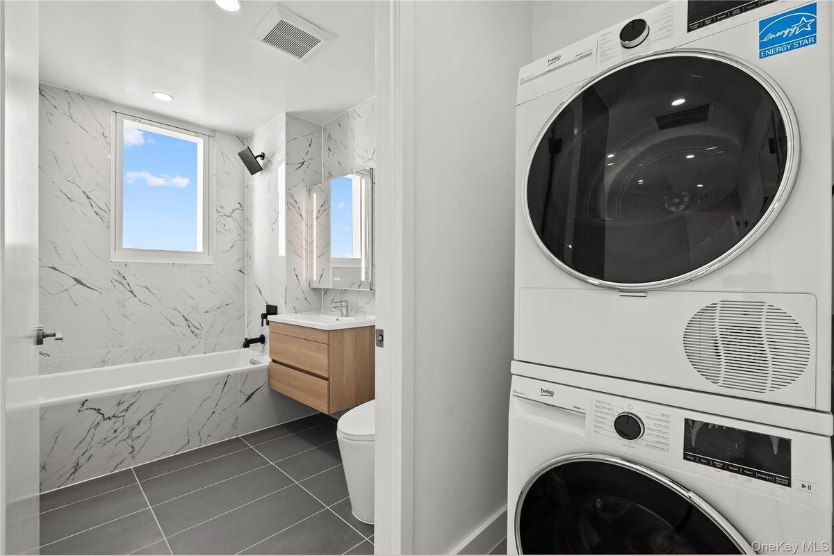 Laundry area with stacked washer / drying machine, recessed lighting, and dark tile patterned flooring