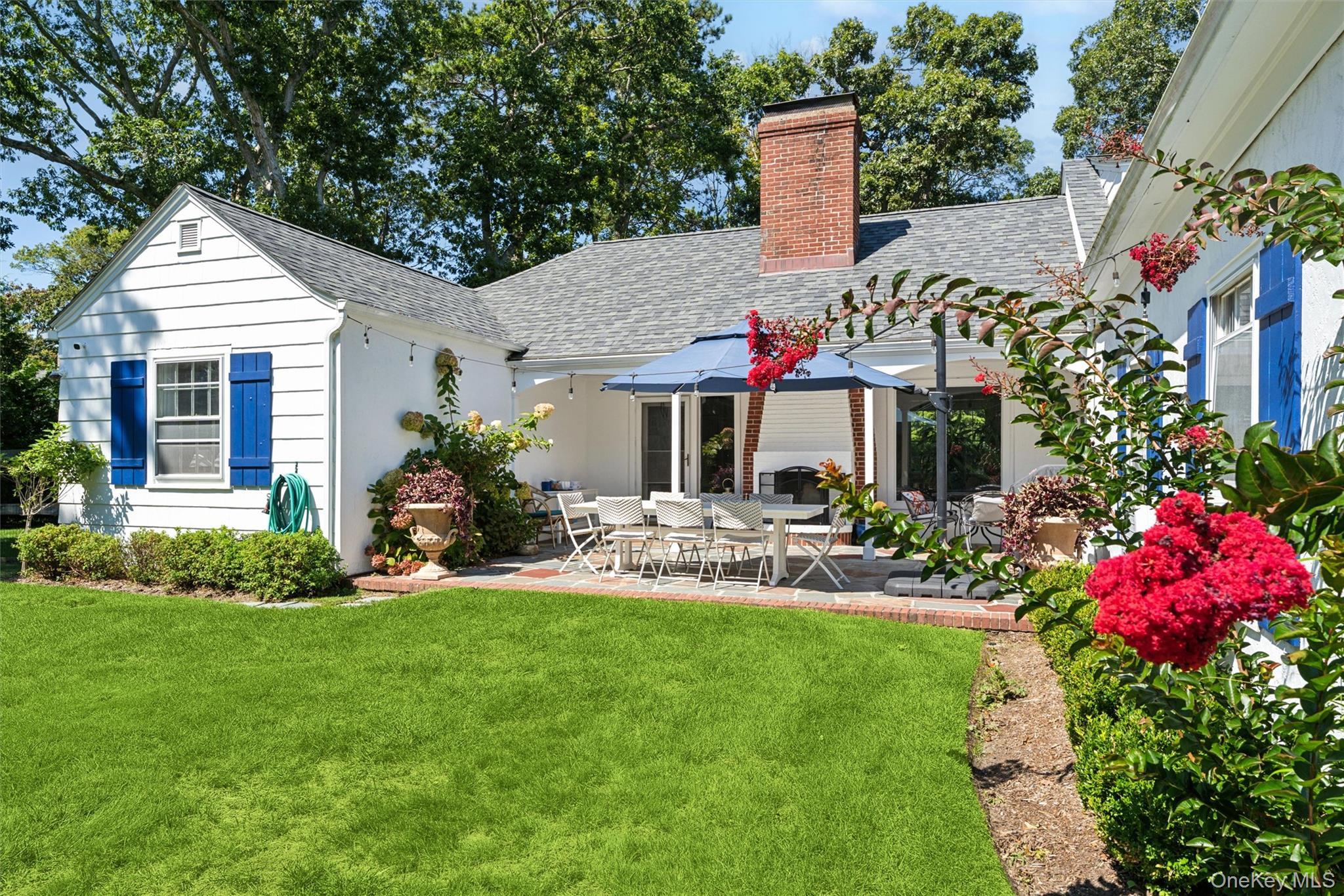 Back of house with a shingled roof, a patio, a chimney, and a lawn