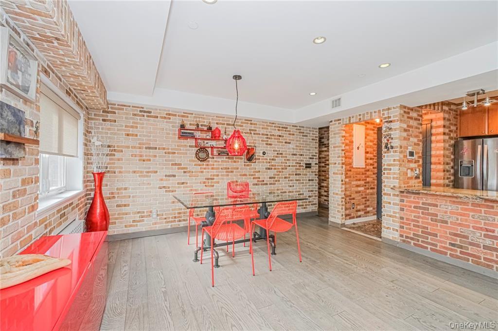 Unfurnished dining area with brick wall, light wood finished floors, a raised ceiling, and recessed lighting