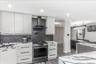 Modern kitchen featuring light wood-finish cabinetry, dark horizontal hardware, and a stainless steel gas range with a coordinating range hood