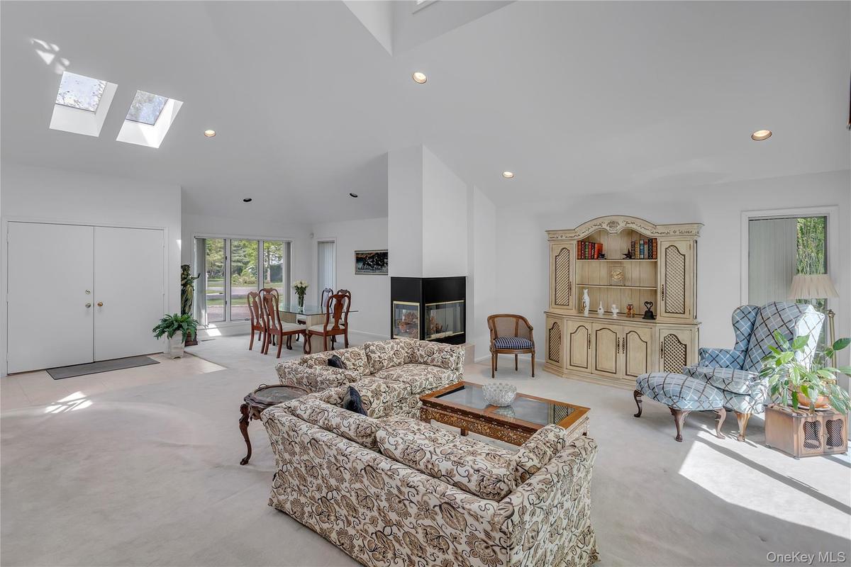 Vaulted ceiling living space featuring dual skylights, recessed lighting, a modern enclosed fireplace, and a dining area with a large window