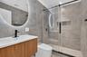 Modern bathroom featuring a wood-finish vanity, integrated sink, and an illuminated circular mirror