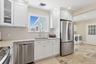 Kitchen with washer and clothes dryer, appliances with stainless steel finishes, white cabinetry, light stone counters, and stone tile floors