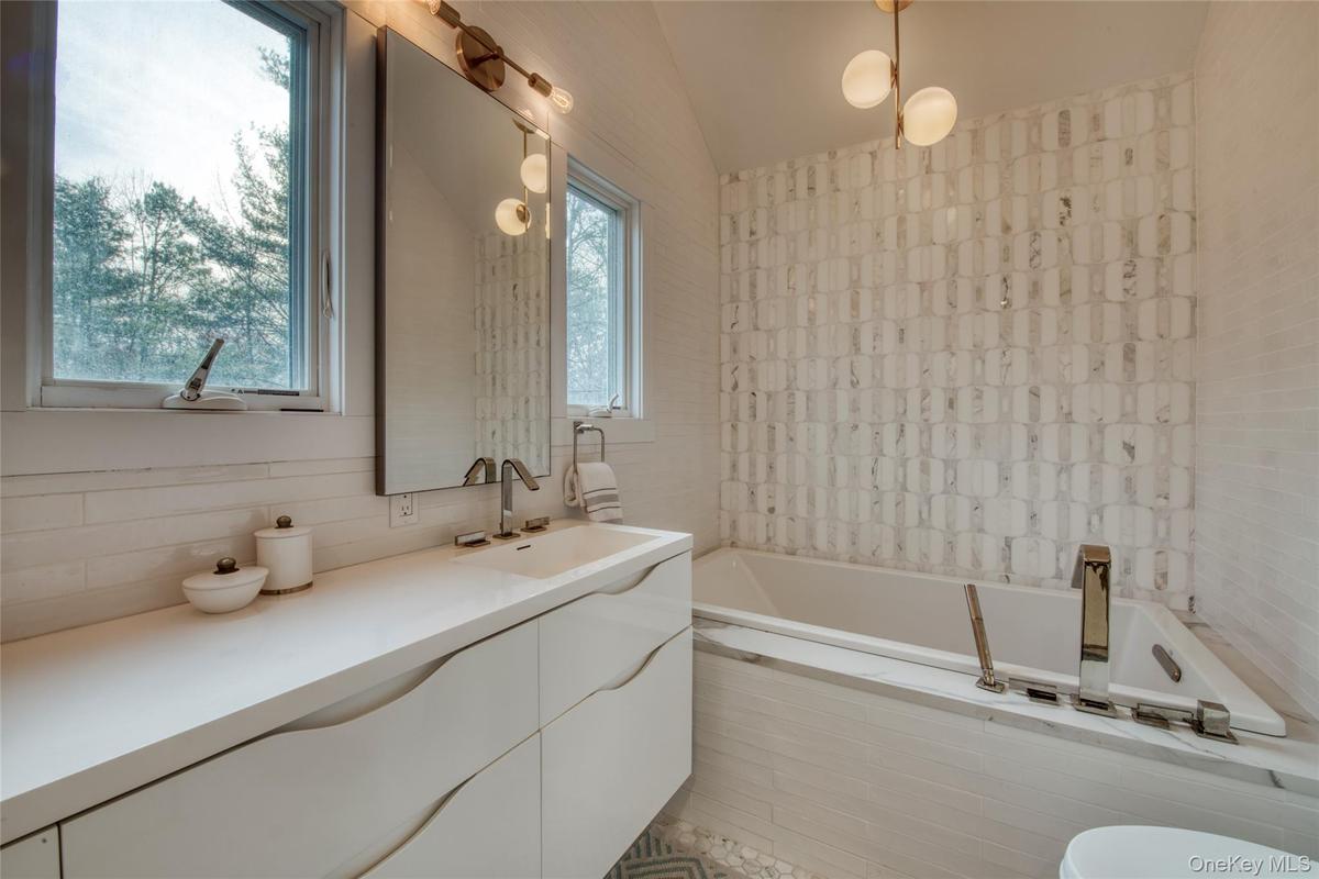 Full bathroom with lofted ceiling, tiled tub, and vanity