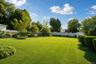 Expansive green lawn with established landscaping, perimeter fencing, and mature trees