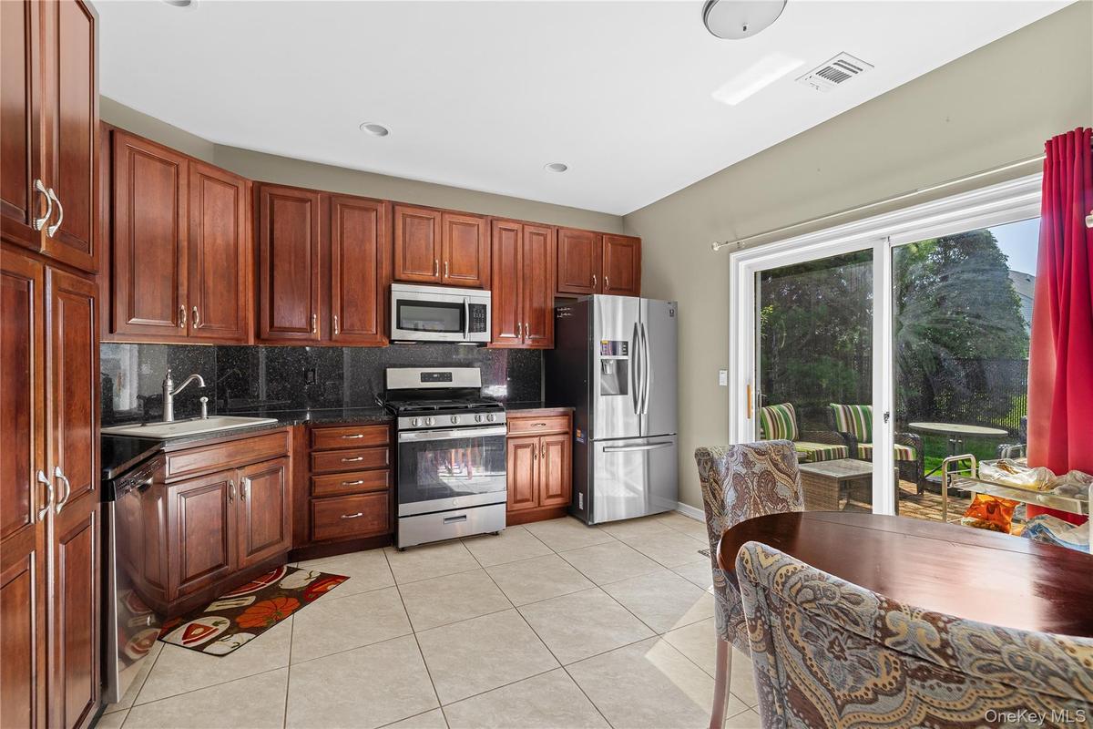 Wood-finish cabinetry with stainless steel appliances, black countertops, and a tile floor