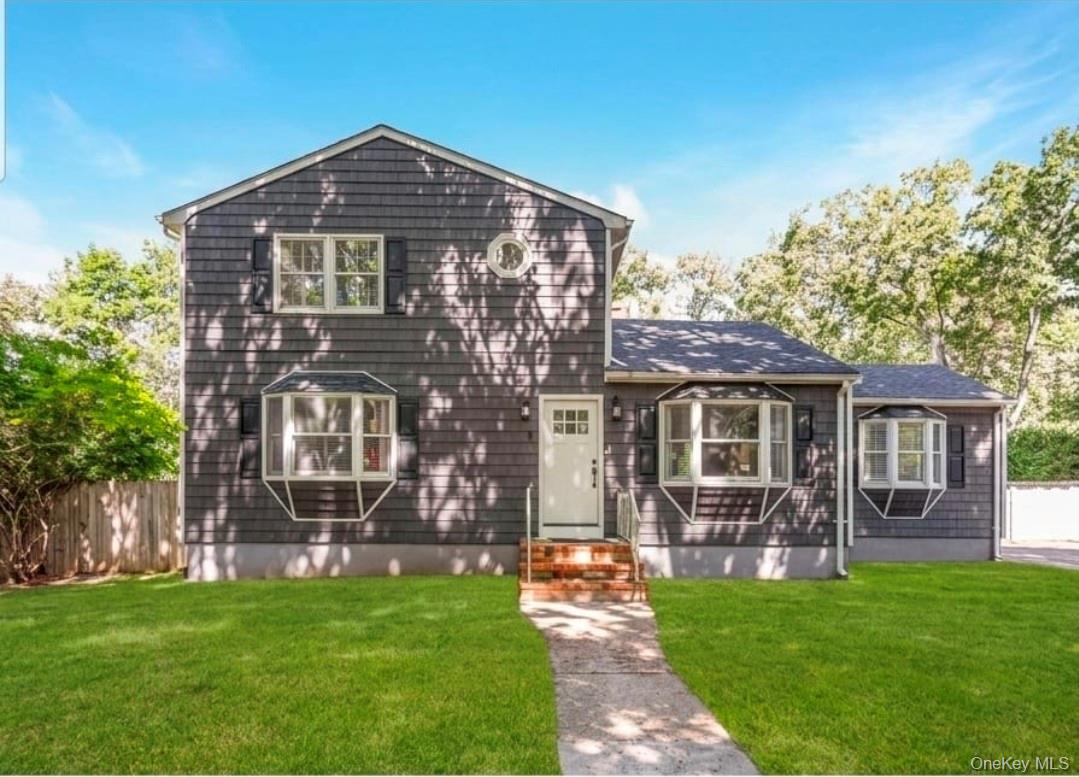 Shingle-sided exterior with a white entry door, three bay windows, black window shutters, and a well-maintained front lawn