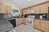 Kitchen with light brown cabinetry, white appliances, vaulted ceiling, tasteful backsplash, and light tile patterned floors