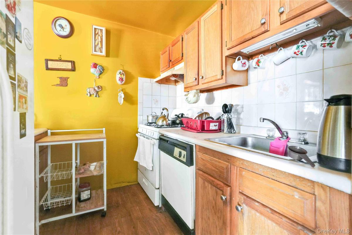 Kitchen with light countertops, backsplash, dark wood-style floors, under cabinet range hood, and white appliances