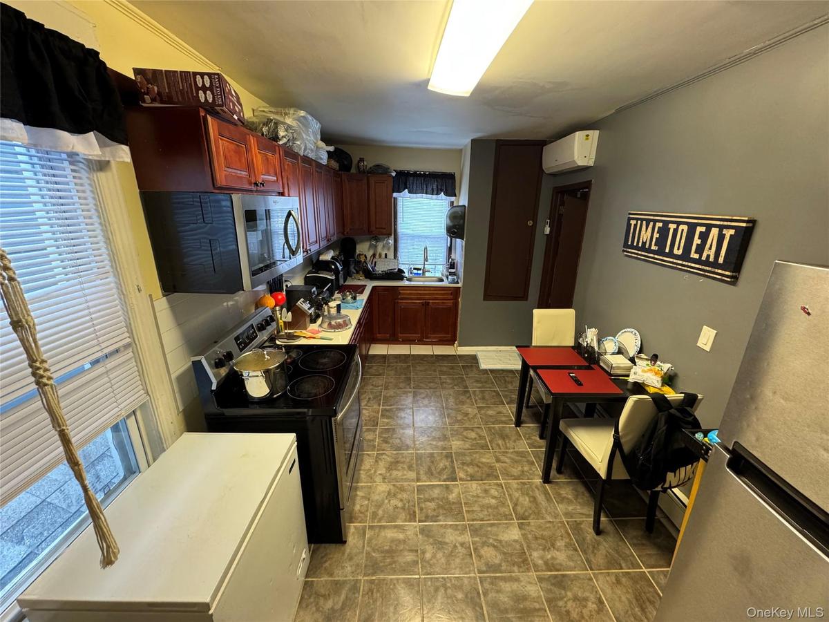 Kitchen with a wall unit AC, stainless steel microwave, electric stove, a sink, and dark brown cabinets