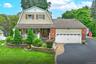 Gambrel roofline with dormer windows, brick and shingle exterior, attached garage with panel door, stone retaining walls, and a paved driveway with pa