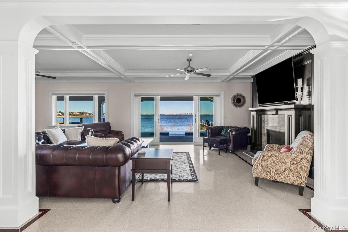 Living room featuring arched walkways, a high end fireplace, ceiling fan, coffered ceiling, and ornate columns