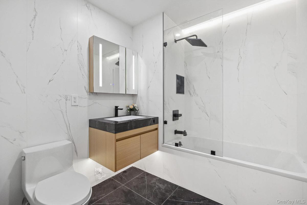 Bathroom with marble tiled floors, vanity, bathtub / shower combination, and toilet