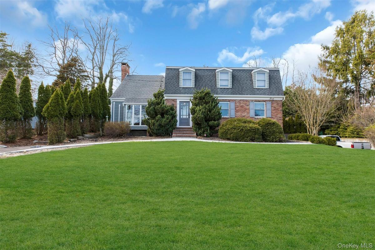View of front of property featuring brick siding, a front lawn, a shingled roof, a chimney, and entry steps