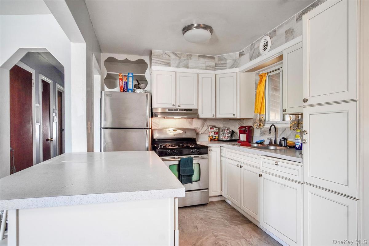 Bright kitchen featuring white cabinetry, a white countertop island, stainless steel appliances, and a marble-patterned tile backsplash