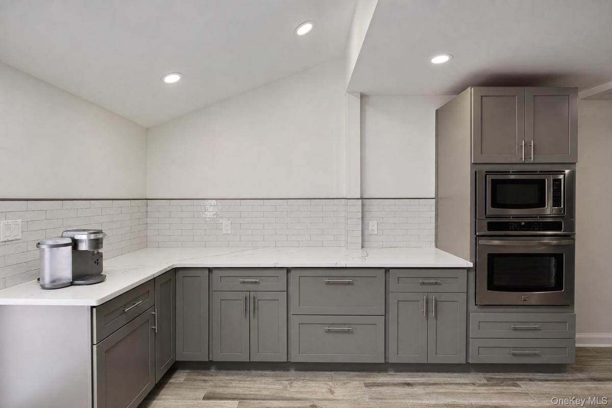 Modern kitchen featuring gray cabinetry, white subway tile backsplash, white countertops, stainless steel built-in appliances, and recessed lighting