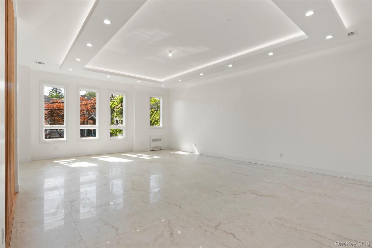 Spare room with light marble finish floors, a tray ceiling, recessed lighting, and radiator