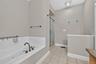 This angle of the primary bathroom shows the shower beyond the soaking tub, with a half wall providing added privacy for the toilet area.