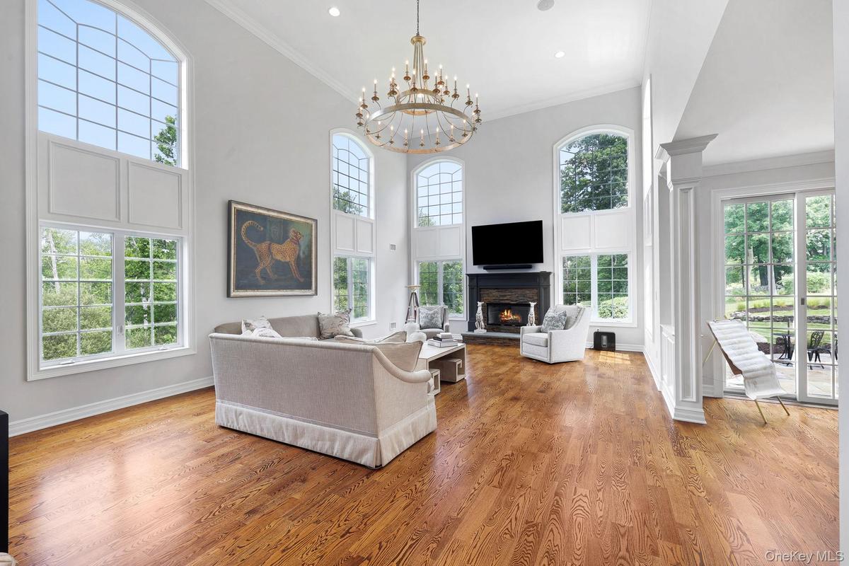 Vaulted ceiling with a large antique chandelier, wood-finish flooring, multiple arched windows, fireplace with a dark mantel, and sliding glass patio 