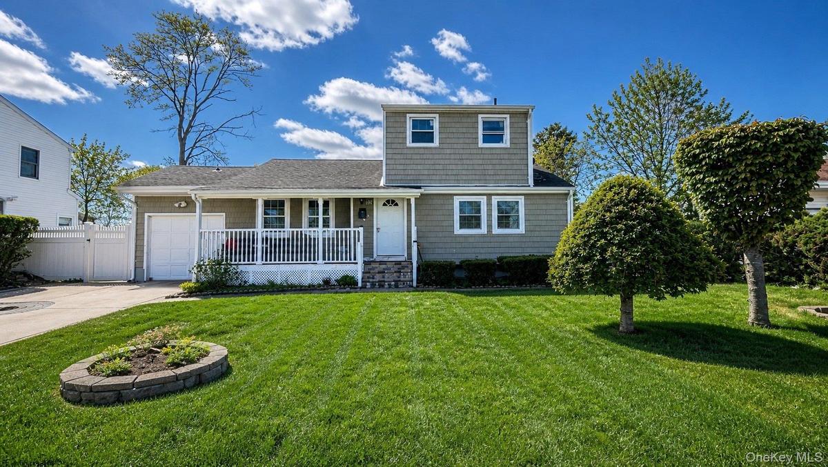 Residential property featuring a siding exterior, covered front porch with white railing, and a driveway leading to an attached garage