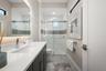 The bathroom has a large vanity, backlit mirror and walk-in shower with glass shower door.