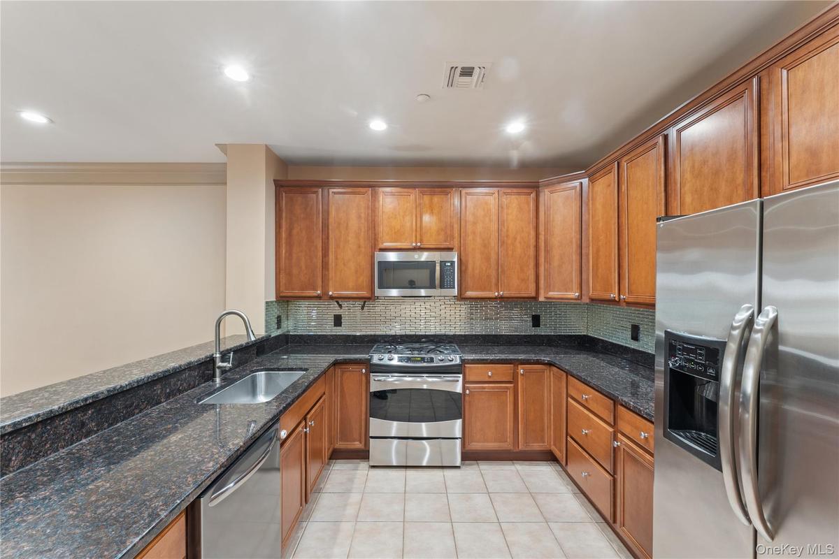 U-shaped kitchen featuring wood cabinetry, dark granite countertops, stainless steel appliances, a tile backsplash, and recessed lighting