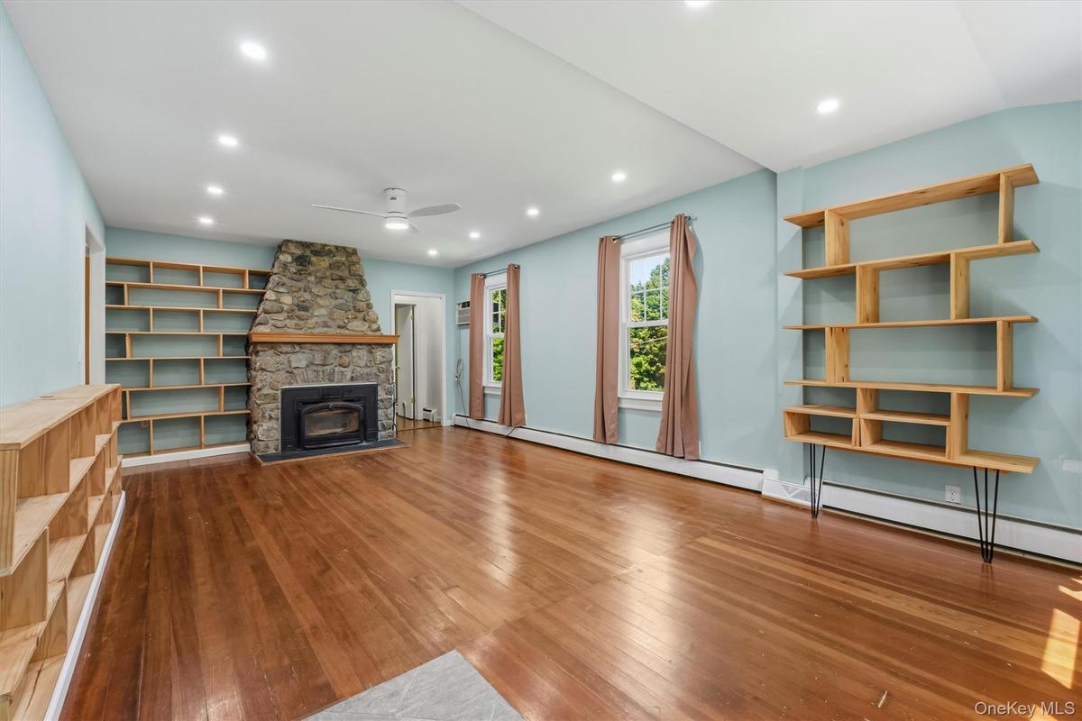 Living area featuring a stone fireplace with a wood mantle, wood-finish flooring, built-in shelving, recessed lighting, and a ceiling fan
