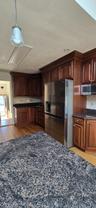 Kitchen featuring rich wood cabinetry with crown molding, stainless steel refrigerator, dark stone countertops, tile backsplash, and wood-finish floor