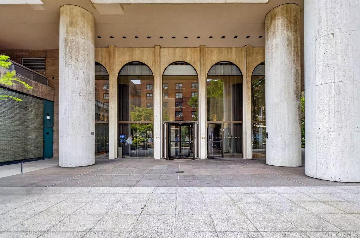 Building entrance featuring large arched windows, a revolving glass door, and substantial cylindrical columns