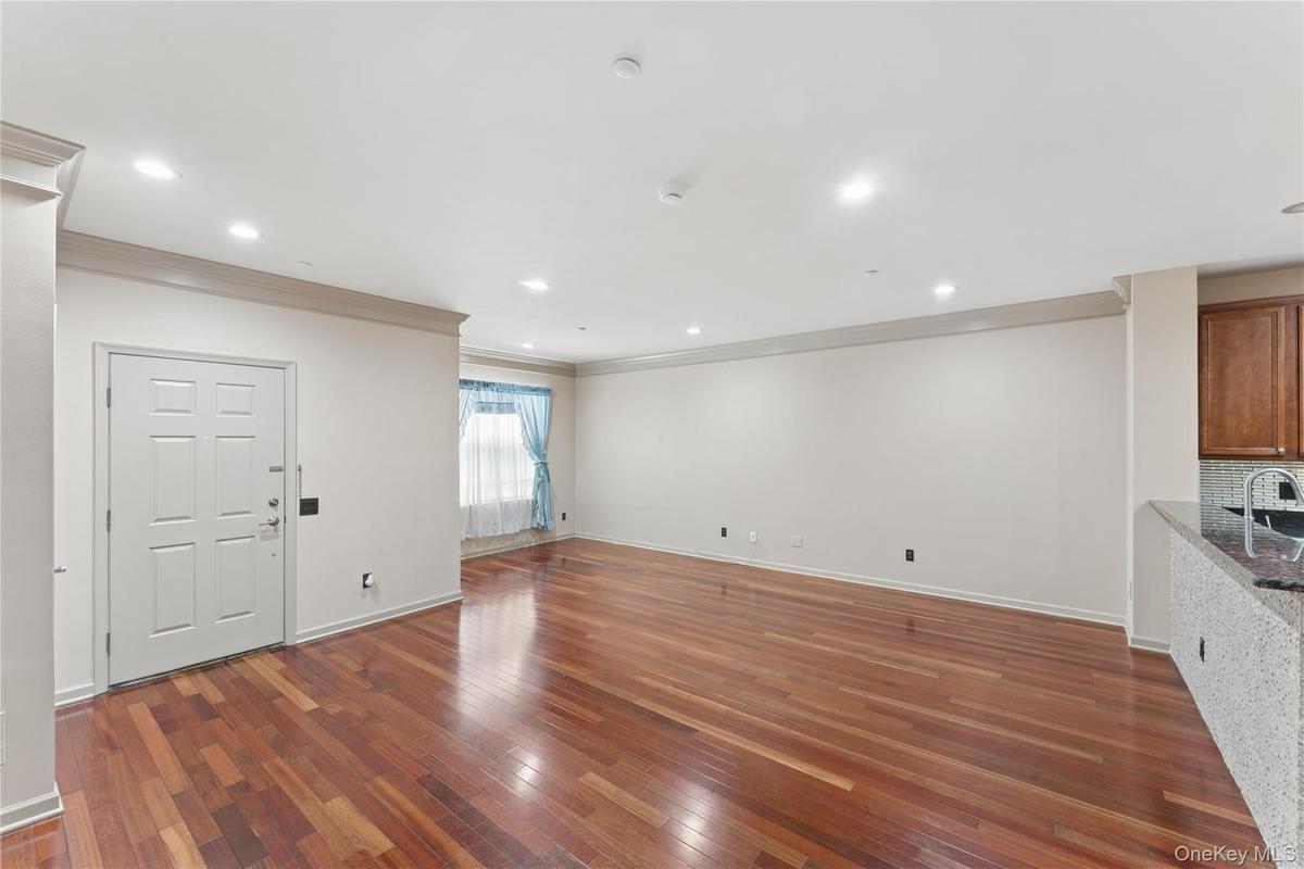 Open-concept living area with polished wood-finish flooring, recessed lighting, crown molding, and a kitchen bar with a granite-style countertop
