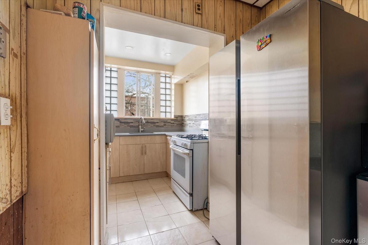 Kitchen featuring white gas stove, a sink, freestanding refrigerator, light brown cabinetry, and light tile patterned floors