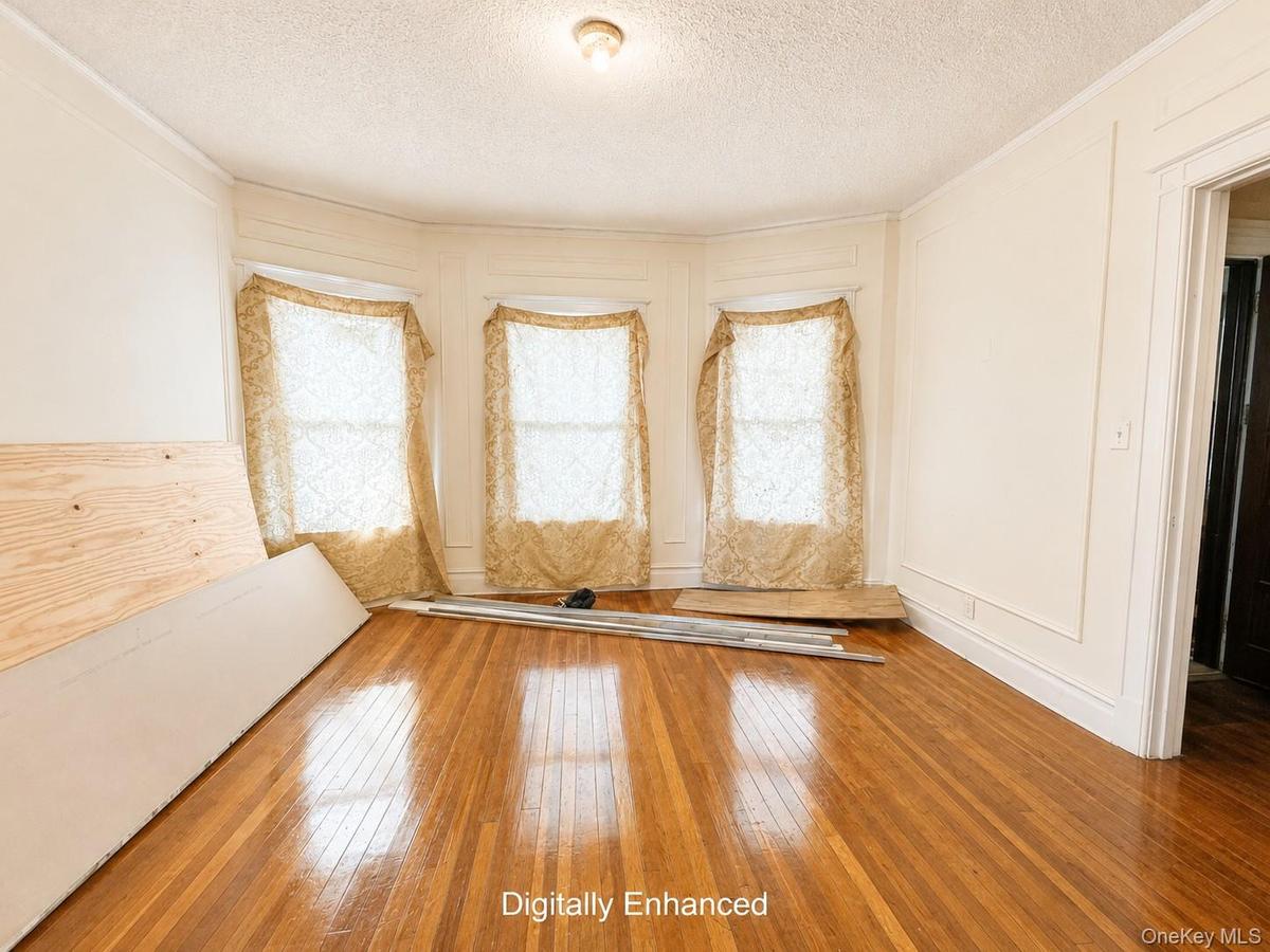 Bay window with three windows, wood-finish flooring, crown molding, and wall paneling