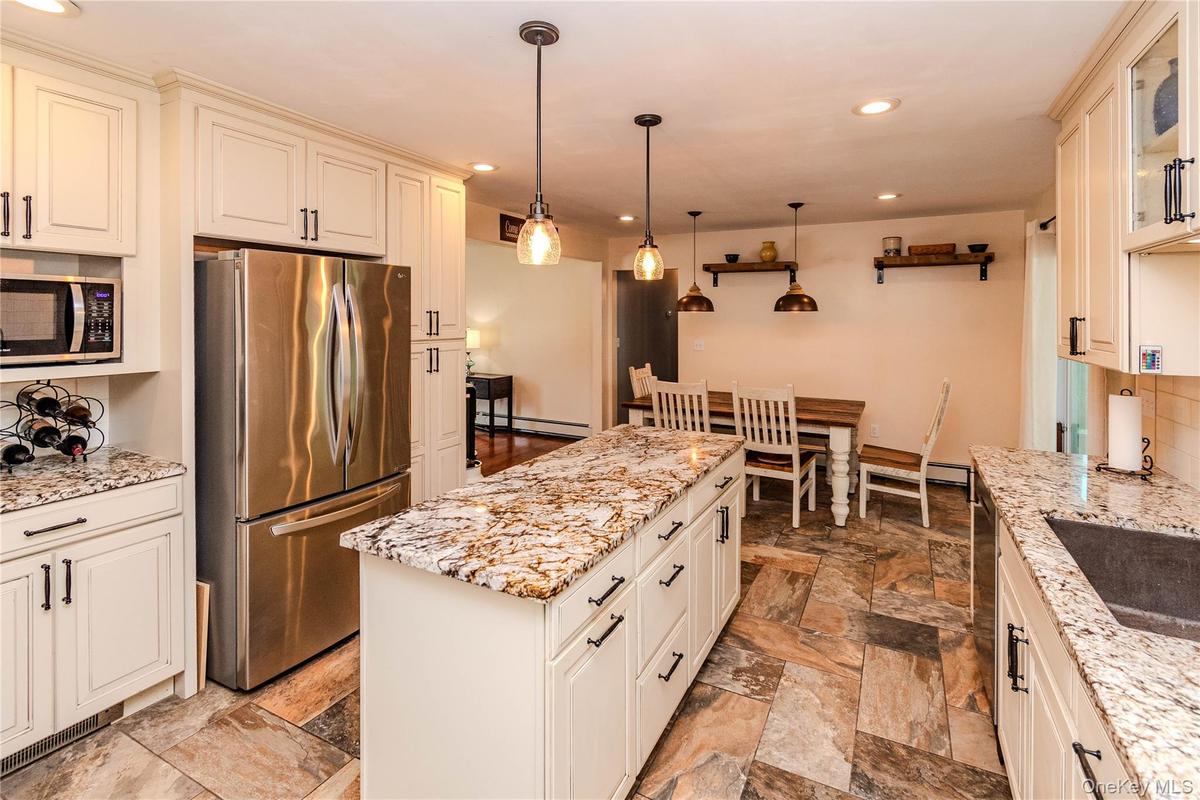 Kitchen featuring extensive cabinetry, stainless steel refrigerator, stone countertops, pendant lighting, and stone tile flooring