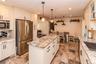 Kitchen featuring extensive cabinetry, stainless steel refrigerator, stone countertops, pendant lighting, and stone tile flooring