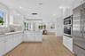 Open-concept kitchen featuring extensive white cabinetry, light wood-finish flooring, stainless steel appliances, and a mosaic tile backsplash