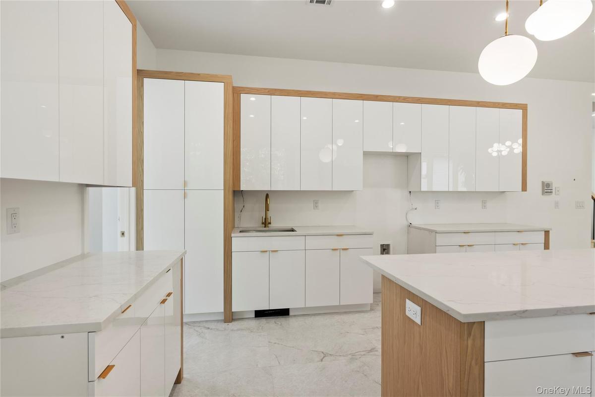 Kitchen featuring white cabinets, light stone countertops, light marble finish flooring, and hanging light fixtures