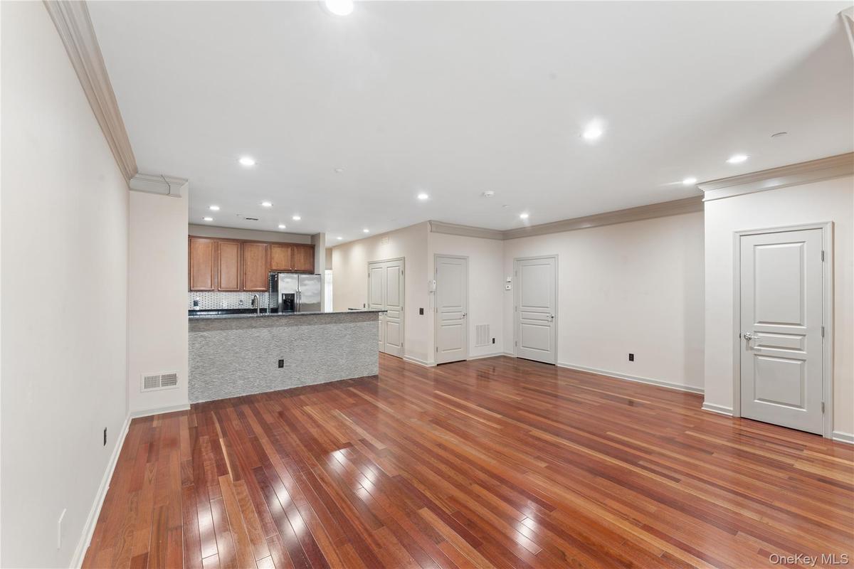 Open-concept living space featuring wood-finish flooring, recessed lighting, crown molding, a kitchen bar with a stone finish, and light wood cabinetr