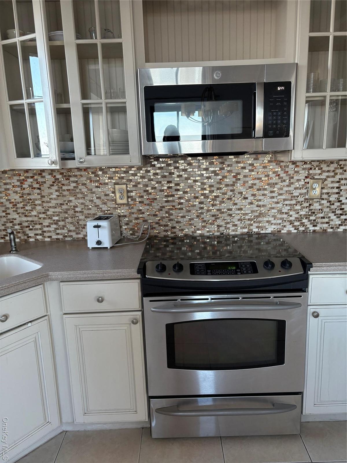 Kitchen with stainless steel appliances, glass insert cabinets, white cabinets, and light tile patterned flooring