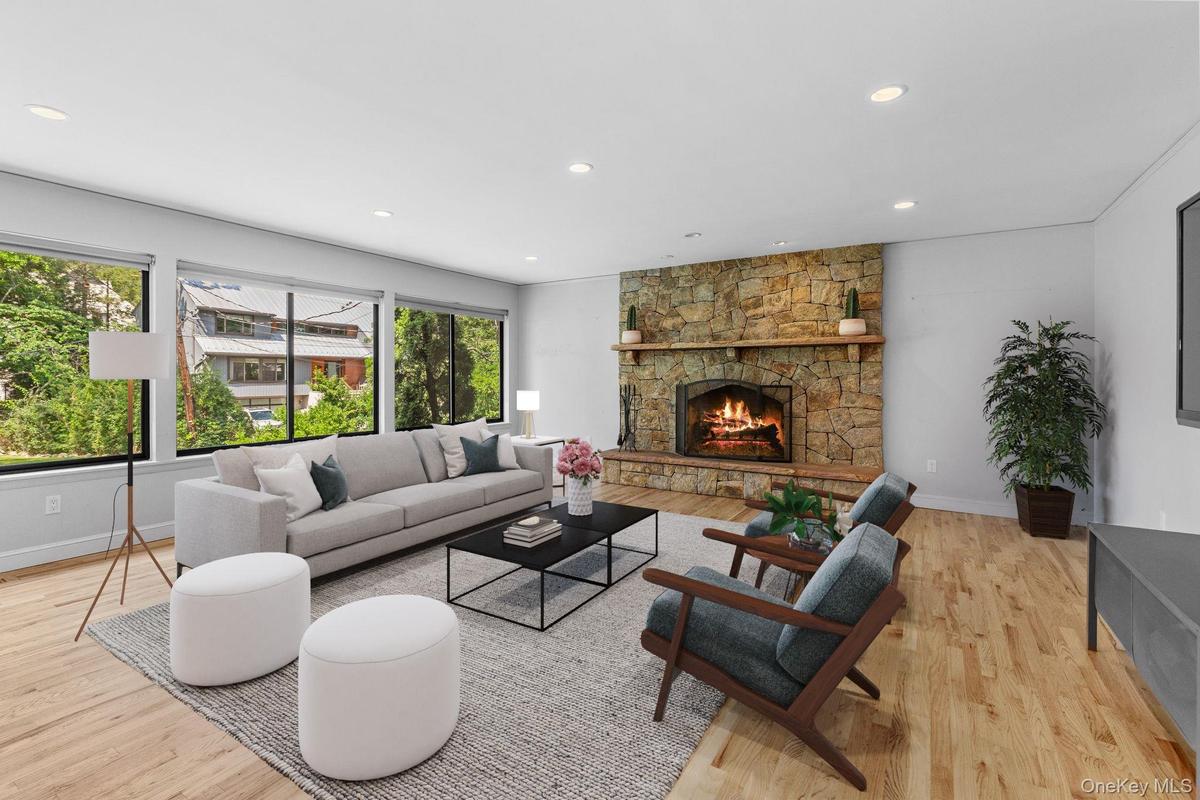Living room with recessed lighting, light wood-style floors, and a stone fireplace (virtually staged)