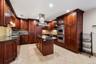 Gourmet kitchen featuring extensive dark wood cabinetry, granite countertops, tile flooring, stainless steel appliances, and a central island with a m