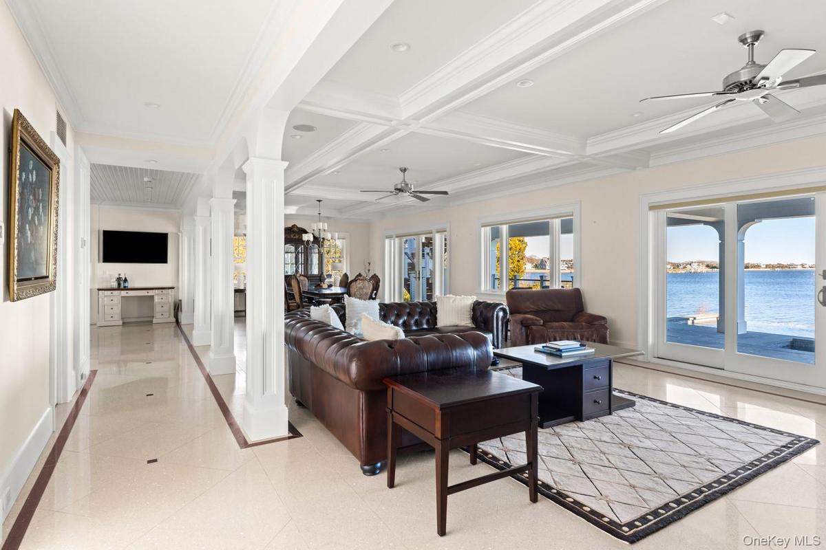 Living room with ceiling fan, decorative columns, ornamental molding, a water view, and coffered ceiling