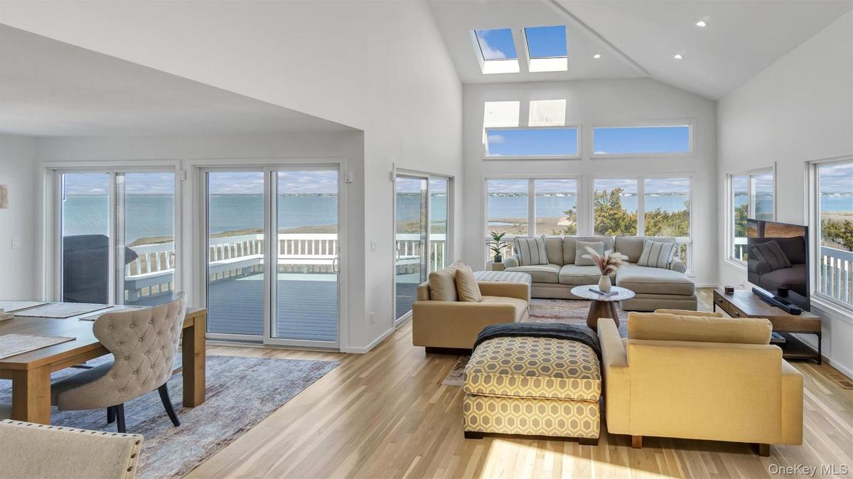Living area with high vaulted ceiling, a skylight, light wood-style floors, and recessed lighting