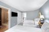 Light-toned wall paint, light wood-finish flooring, white paneled doors, and an en-suite bathroom with a glass-enclosed shower over tub