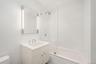 Bathroom featuring a vanity with an integrated sink and chrome fixtures, illuminated mirror with vertical lighting, floor-to-ceiling white tiled walls