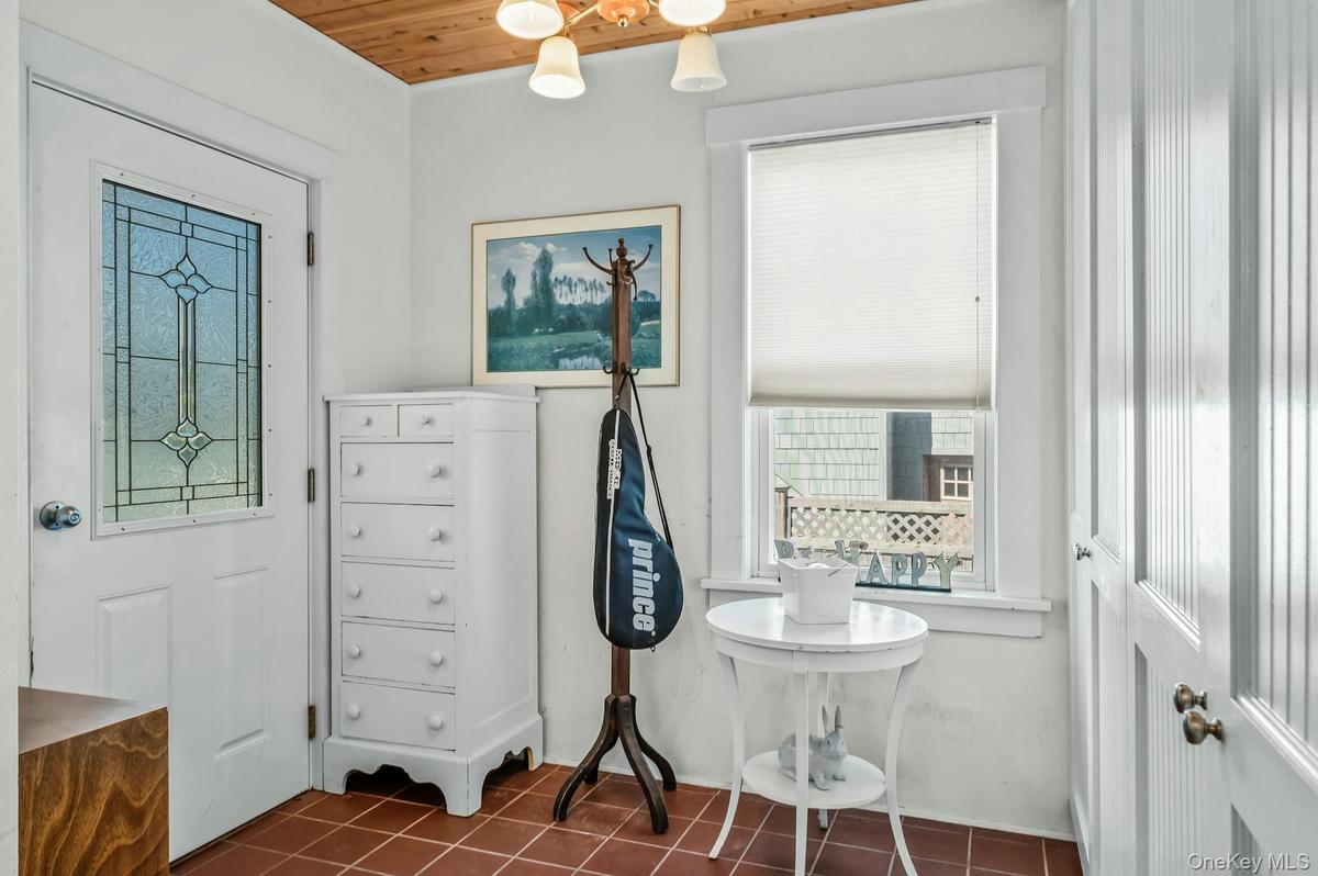 Entry area featuring terracotta-style tile flooring, a wood-paneled ceiling, and a white paneled door with decorative glass