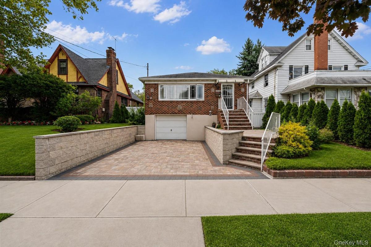 Brick exterior with a white garage door, paved driveway, and stone retaining walls