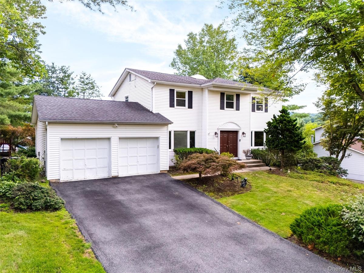 White siding exterior with a two-car garage, asphalt driveway, mature trees, and a landscaped front yard