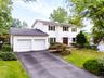 White siding exterior with a two-car garage, asphalt driveway, mature trees, and a landscaped front yard
