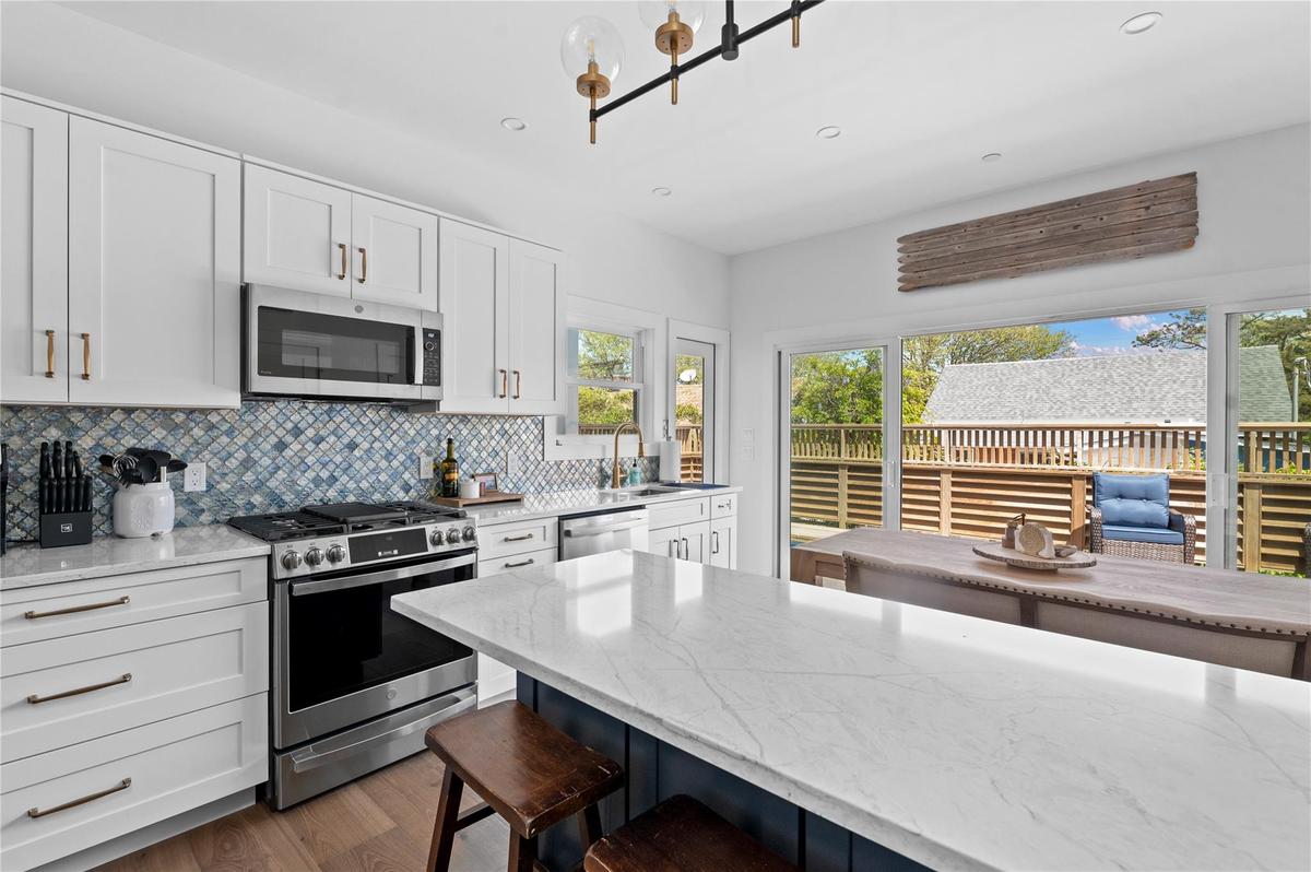 Kitchen featuring appliances with stainless steel finishes, a breakfast bar, tasteful backsplash, light stone countertops, and wood finished floors